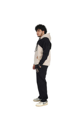 Person wearing a black and beige hoodie with black pants on a white background